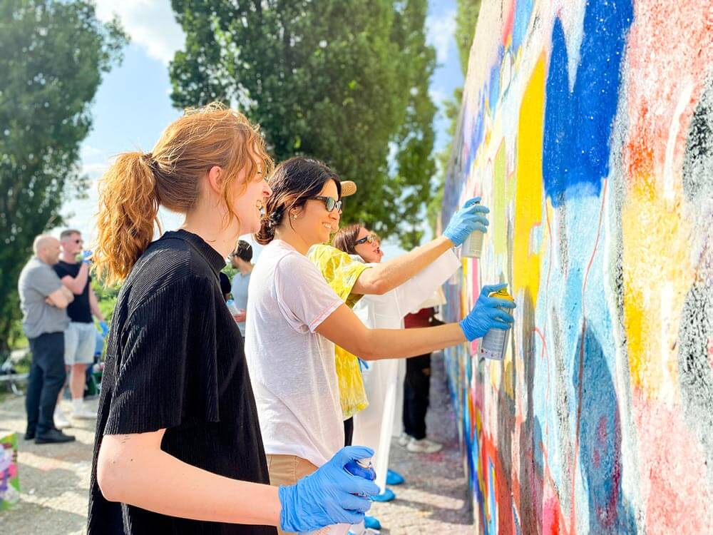 Diverse Firmengruppe bei der Zusammenarbeit an einem großformatigen Wandbild, die beste Idee für ein Team-Event in Berlin.