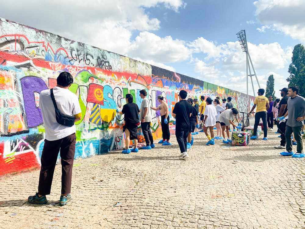 Team von Mitarbeitern bei einem kreativen Graffiti-Workshop in Berlin, die gemeinsam eine farbenfrohe Wand gestalten – Teambuilding, Zusammenarbeit und Kreativität